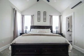 Ein Schlafzimmer mit einem dunklen Holzbett, zwei Nachttischen, einem großen Fenster mit Vorhängen und einem Deckenventilator.