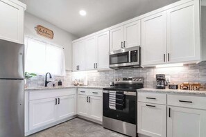 A modern kitchen with white cabinets, stainless steel appliances, and a window with a white curtain.