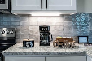 Eine Küche mit weißen Schränken, einer Kaffeemaschine, einem Filterhalter und Kaffee-Dekorationen aus Holz.