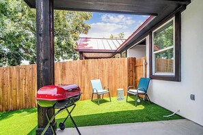Ein Garten mit Kunstgrasanlage, einem Grill, zwei Stühlen und einem Holzzaun.