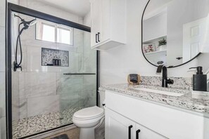 A modern bathroom with a glass shower enclosure, a white toilet, a granite countertop, and a large mirror. - Pet Friendly w/Hot-Tub-Six Minutes to Downtown! (Fredericksburg)