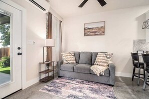 Ein Wohnzimmer mit grauem Sofa, einem gemusterten Teppich, einer Lampe und einem Gemälde an der Wand.
