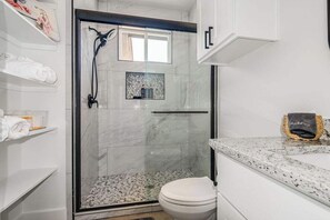A modern bathroom with a glass shower enclosure, a toilet, and marble countertops.