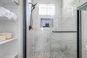 Ein modernes Badezimmer mit einer Duschkabine aus Glas, Marmorfliesen, einem Handtuchhalter und einem Ablagefach für Toilettenartikel.