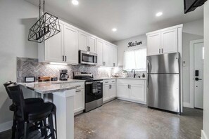 A modern kitchen with white cabinets, stainless steel appliances, a herringbone tile backsplash, and a bar area with stools. - Pet Friendly w/Hot-Tub-Six Minutes to Downtown! (Fredericksburg)