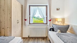 Un dormitorio con un armario de madera, una ventana con cortinas, una cama con almohadas y una mesita de noche con lámpara.