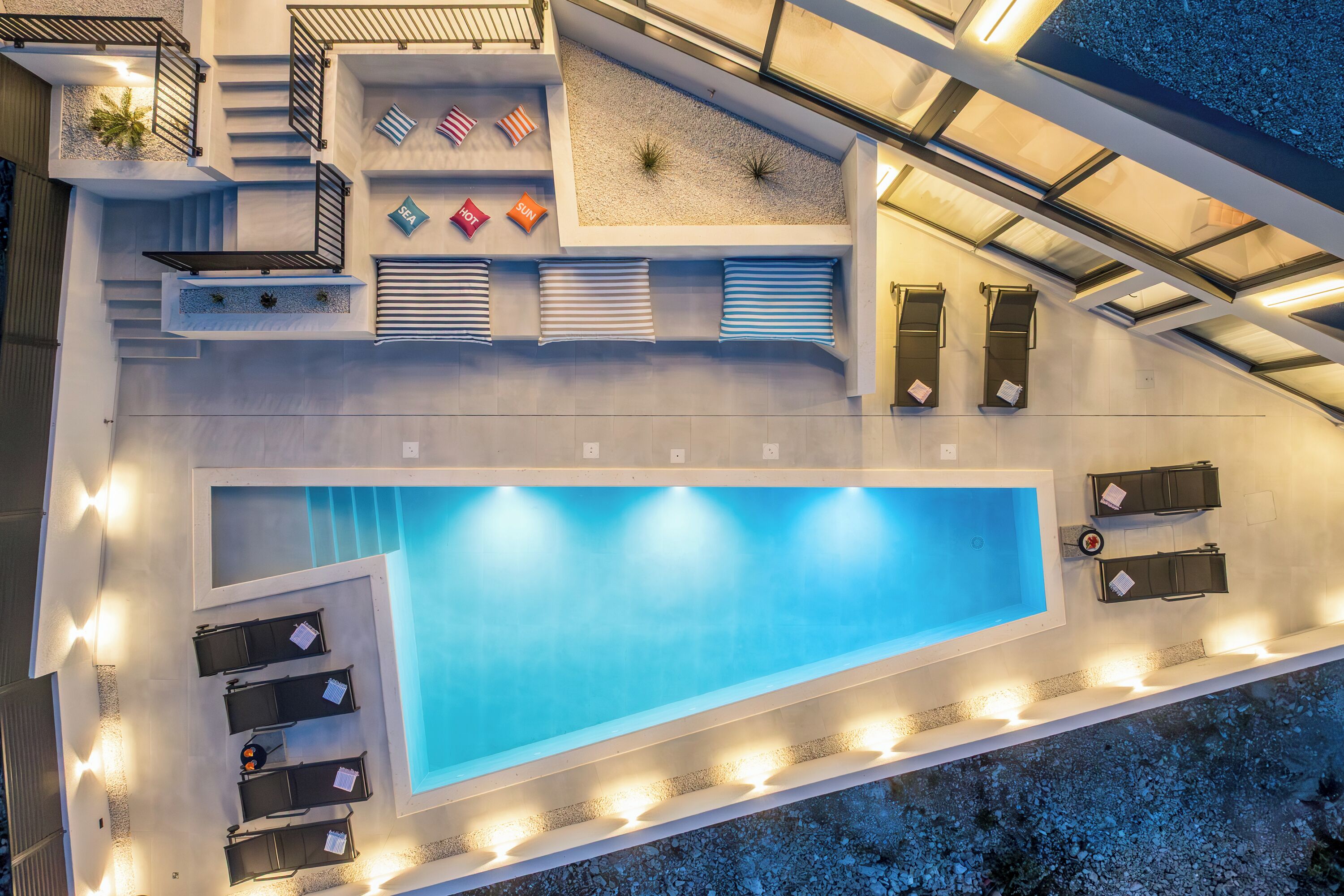 Eine Vogelperspektive auf einen Poolbereich auf einem Dach mit einem großen Pool, Liegestühlen und einer Treppe, die zu einem Balkon führt.