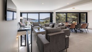 A modern living room with a large TV, comfortable seating, and a dining area with a view of the sea. - Mar Escape Designer Villa Croatia w/Sea Views, Private Pool, 4 En-Suite Bedrooms (Vinišće)