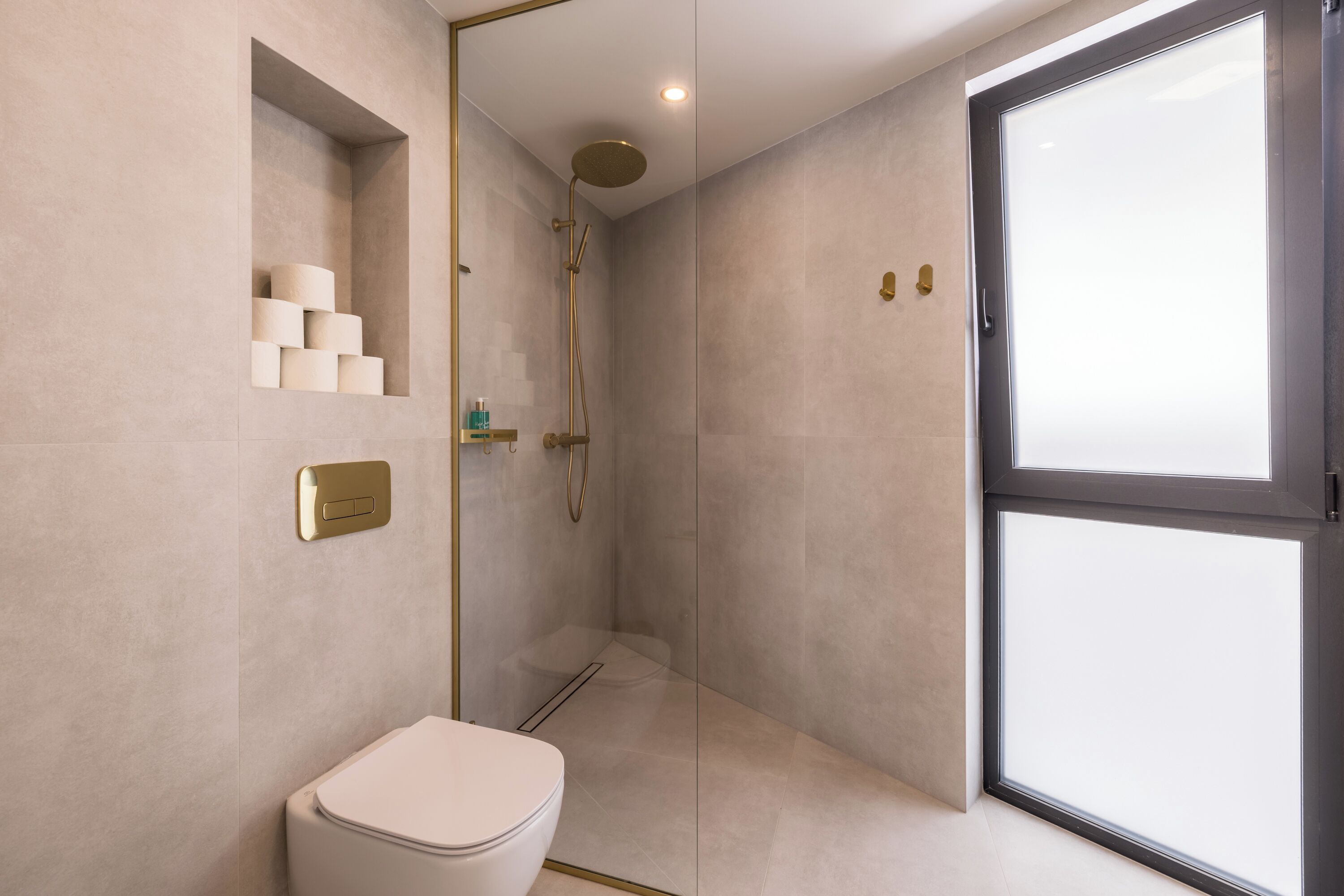 A modern bathroom with a toilet, a shower, and a glass door leading to a balcony.