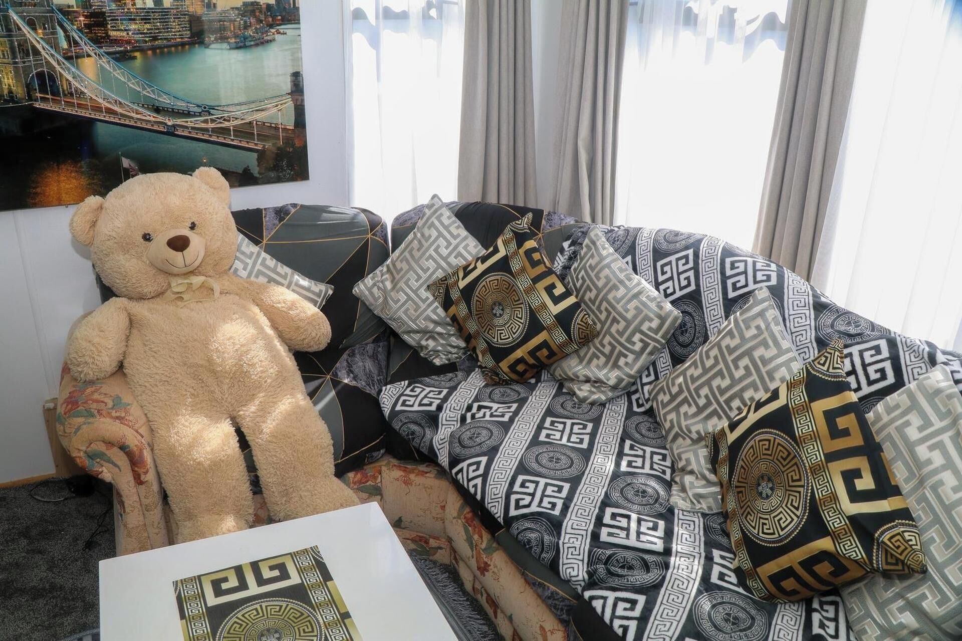 A bed with patterned bedding, a teddy bear, and a framed picture of a bridge.