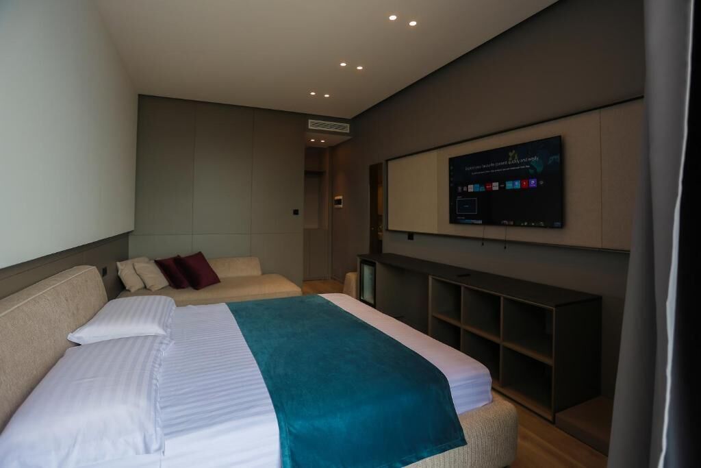A modern hotel room with a large bed, a television mounted on the wall, and a built-in shelving unit.