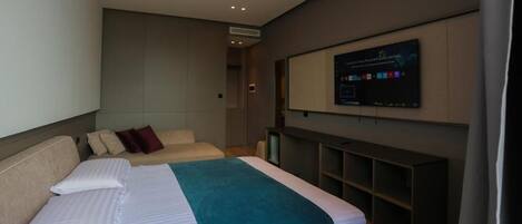 A modern hotel room with a large bed, a television mounted on the wall, and a built-in shelving unit.
