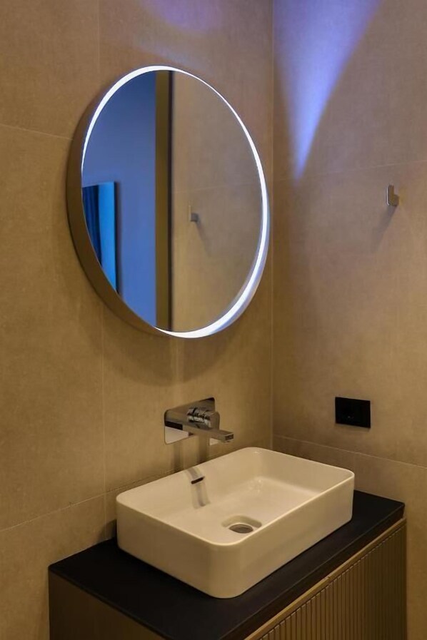A bathroom with a round mirror, a white sink, and a black countertop.