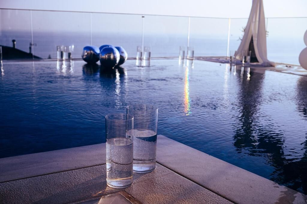 An infinity pool with clear water, two glasses of water, and a modern bridge structure in the background.