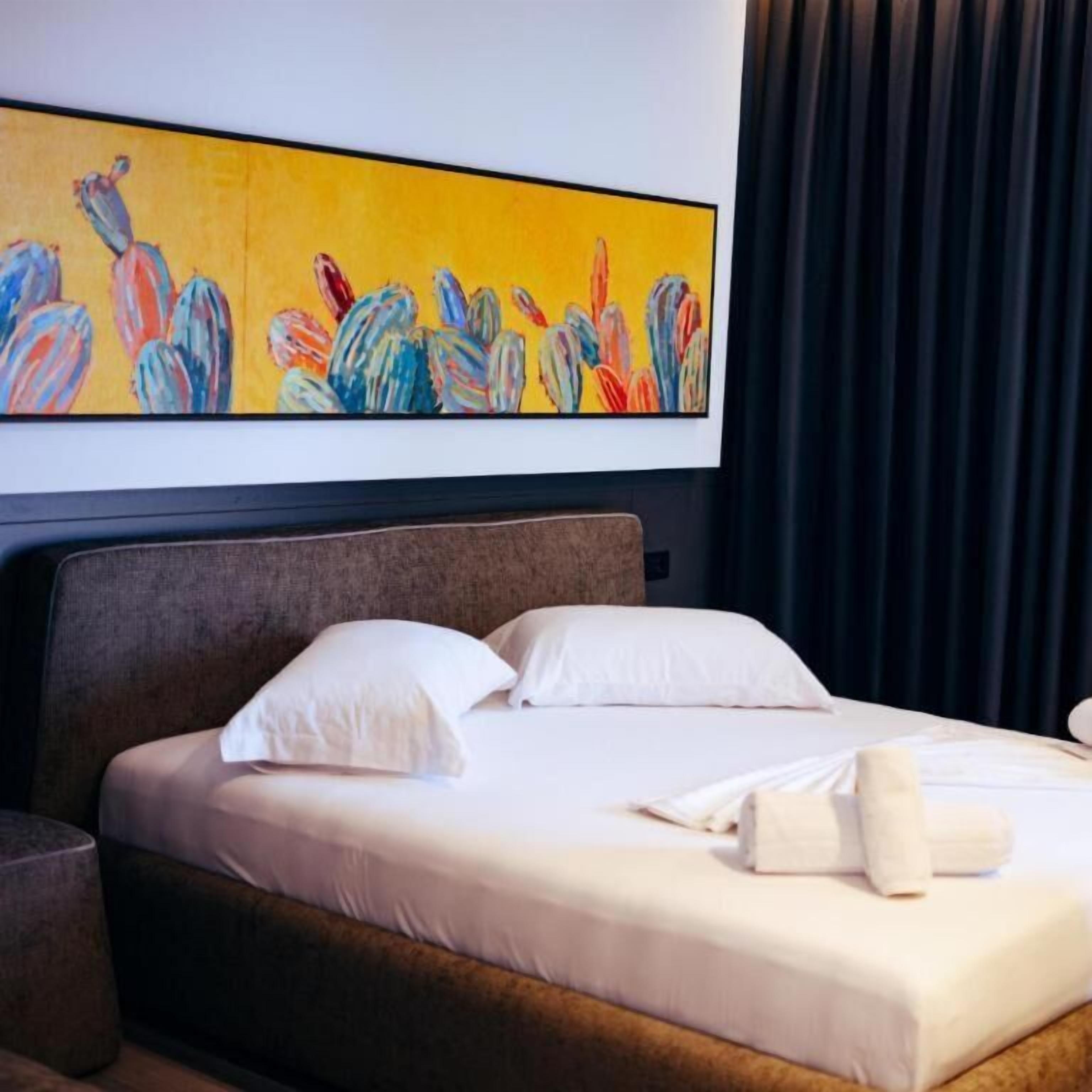 A hotel room with a bed, pillows, a headboard, and a painting above the bed.