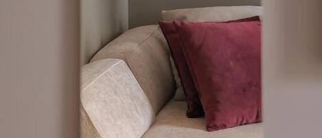 Un rincón de una habitación con un sofá color beige y un cojín rojo.