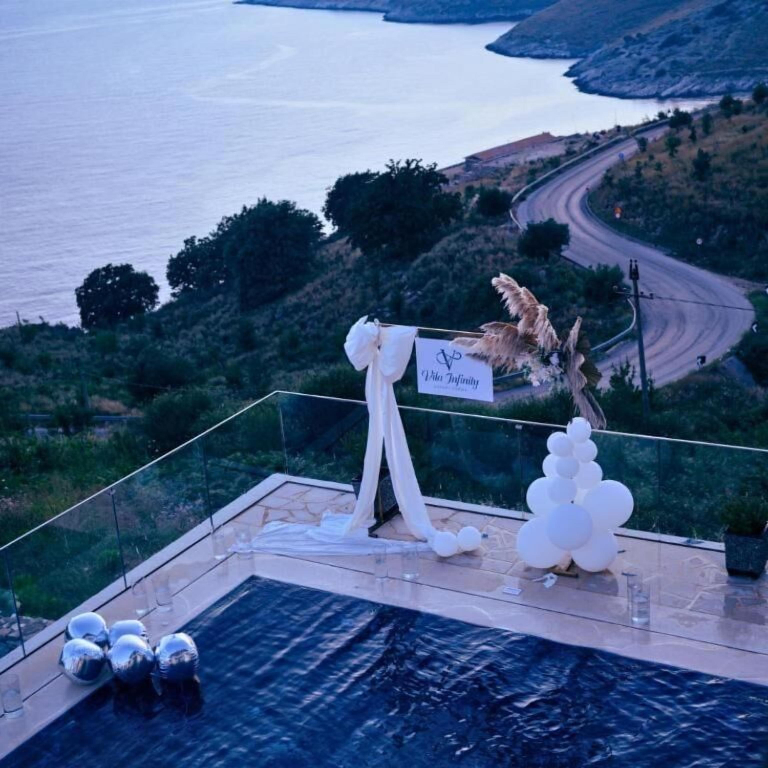 Una terraza en la azotea con piscina, un letrero que dice 'Villa Infinity' y vistas al mar y las colinas.