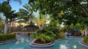 Un área de piscina con una palmera, sillones de descanso y un puente.