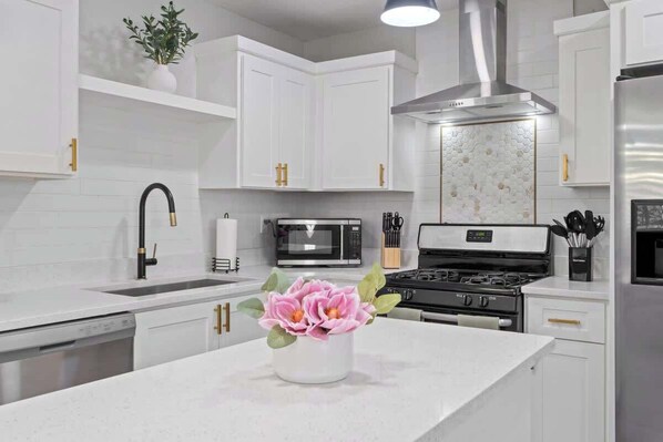 A modern kitchen with white cabinetry, stainless steel appliances, and a central island with a vase of flowers.
