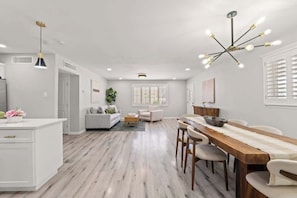 A modern kitchen with white cabinetry, a wooden dining table, and a chandelier.