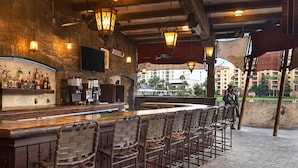 An outdoor bar area with brick walls, a wooden bar counter, and multiple bar stools. - 3BD/Orlando Near Disney - 5 Pools, Game Room, Café and Restaurant On-Site! (Lake Buena Vista)