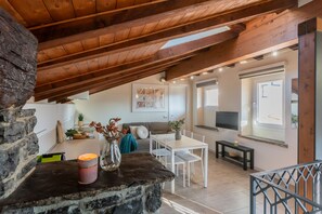 A cozy interior with a stone fireplace, wooden ceiling beams, a dining area, and a living space with a TV and artwork.