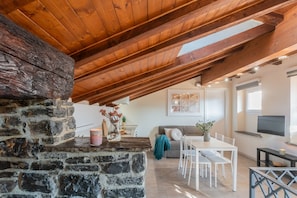 A cozy dining area with a stone fireplace, wooden ceiling beams, a white dining table, and a TV mounted on the wall. - Domus 5 in Como in Como (Como)