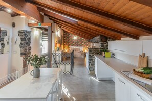 Una cocina moderna con paredes de piedra, vigas de madera y un comedor con mesa y sillas blancas.