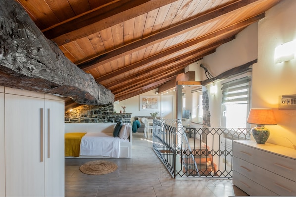 A cozy room with a wooden ceiling, stone wall, white furniture, and a view of the outdoors.