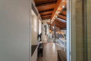 A hallway with wooden beams, a bench, a TV mounted on the wall, and a dining area with a table and chairs.