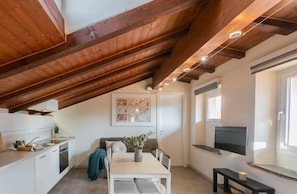A modern kitchen with white cabinets, a dining area with a table and chairs, a sofa, and a TV mounted on the wall.