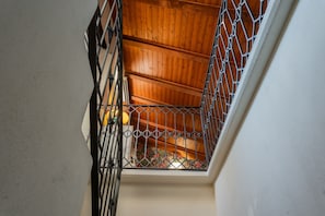 A staircase with a metal railing, wooden steps, and a view of a room with patterned carpet.