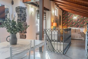 Un comedor con una mesa y sillas, una planta en maceta, un muro de piedra y una escalera que lleva a una sala de estar con un diseño floral en la pared.