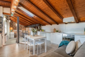 A modern kitchen with white cabinets, a wooden ceiling, and a dining area with a white table and chairs. - Domus 5 in Como in Como (Como)