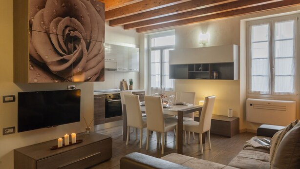 Una sala moderna con un televisor de pantalla plana, un comedor con mesa y sillas, un sofá y una gran obra de arte floral en la pared.