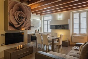 Ein modernes Wohnzimmer mit Flachbildfernseher, einem Essbereich mit Tisch und Stühlen, einer Couch und einem großen Blumenbild an der Wand.