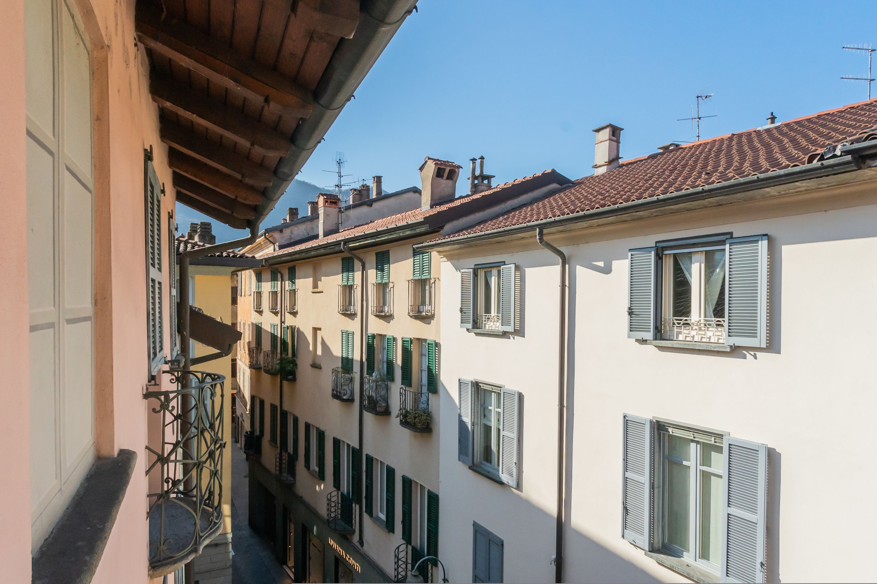 A narrow street with buildings featuring balconies and shutters.