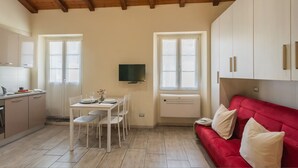 Cocina compacta con una mesa y sillas, un sofá rojo y un televisor montado en la pared.