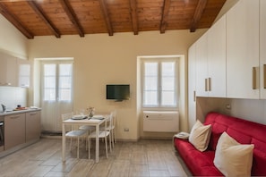 A compact kitchen with a dining table and chairs, a red sofa, and a television mounted on the wall. - Domus 3 in Como in Como (Como)