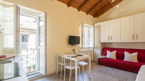 Un espacio habitable compacto con comedor, un sofá rojo y televisor montado en la pared.
