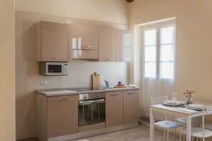 A modern kitchen with beige cabinets, a microwave, and an oven. There is a dining area with a table and chairs. - Domus 3 in Como in Como (Como)