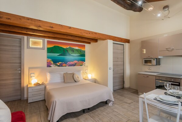 Une chambre à coucher comprenant un lit, des tables de chevet, un tableau et un coin cuisine.
