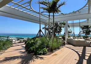A covered outdoor area with a wooden deck, seating, and a view of the ocean. - Miami 72 Building - 360-degree Views - We host (Miami Beach)