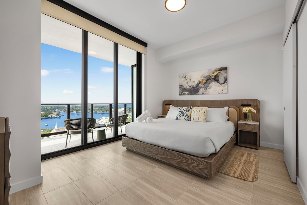Un dormitorio moderno con una cama grande, vistas al mar y un balcón con mobiliario exterior.