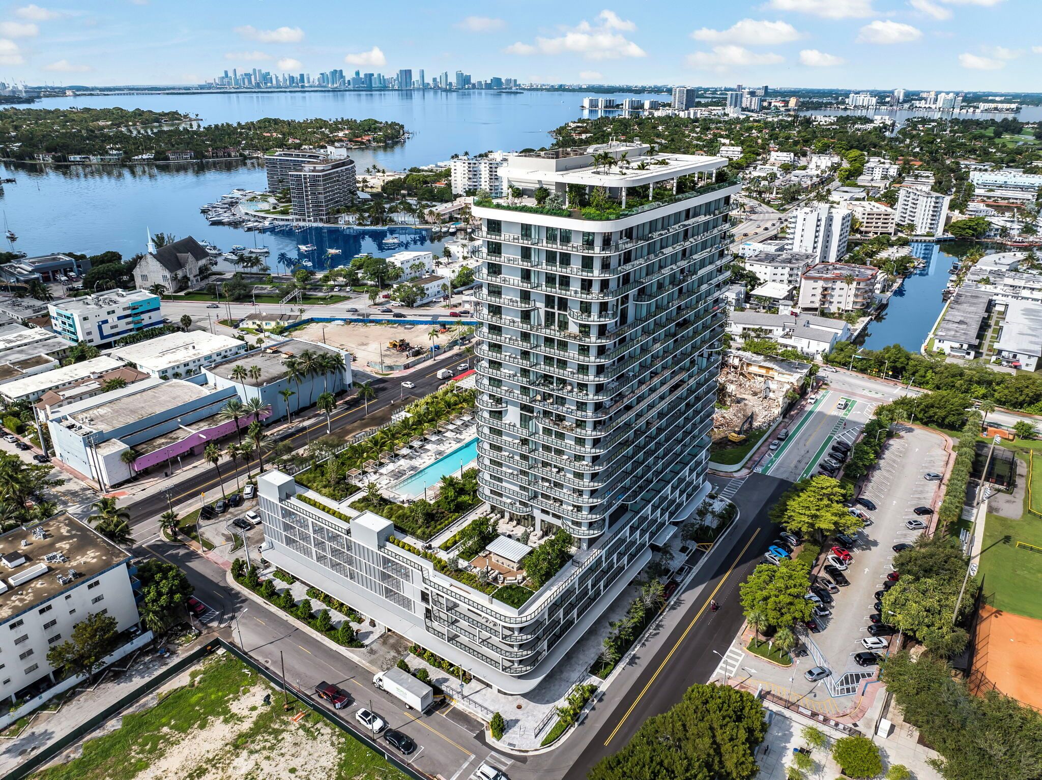 A high-rise hotel with a rooftop pool, surrounded by a marina and city skyline.