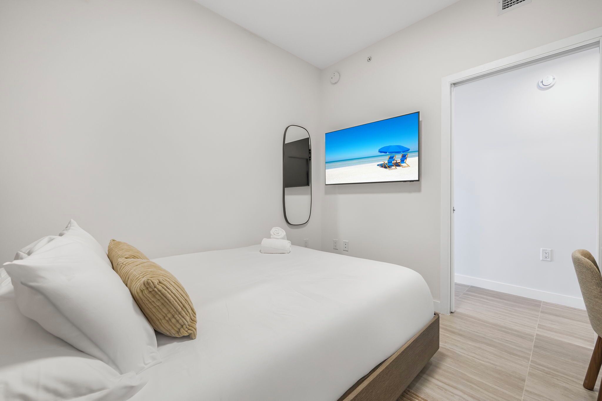 Una camera d'albergo moderna con un letto grande, una TV a schermo piatto montata a parete, uno specchio e una porta.