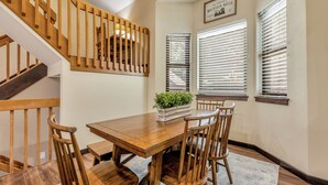 Un comedor con una mesa y sillas de madera, una escalera con barandillas de madera y una planta en maceta sobre la mesa.