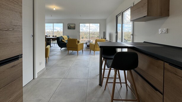 A modern kitchen with a dining area, featuring a large window, wooden cabinets, and a black countertop.