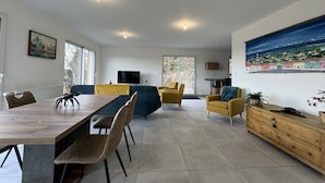 A spacious living area with a dining table, yellow chairs, a sofa, and a large painting on the wall.