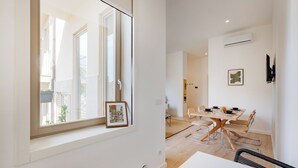 A modern dining area with a wooden table and metal chairs, a window with a framed picture, and an air conditioning unit on the wall. - The Superior Green at BoaVista Flats (Porto)